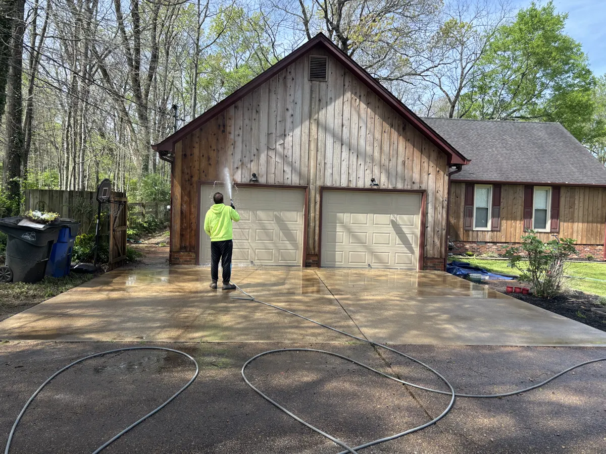 House washing in progress on wood siding above a residential garage.