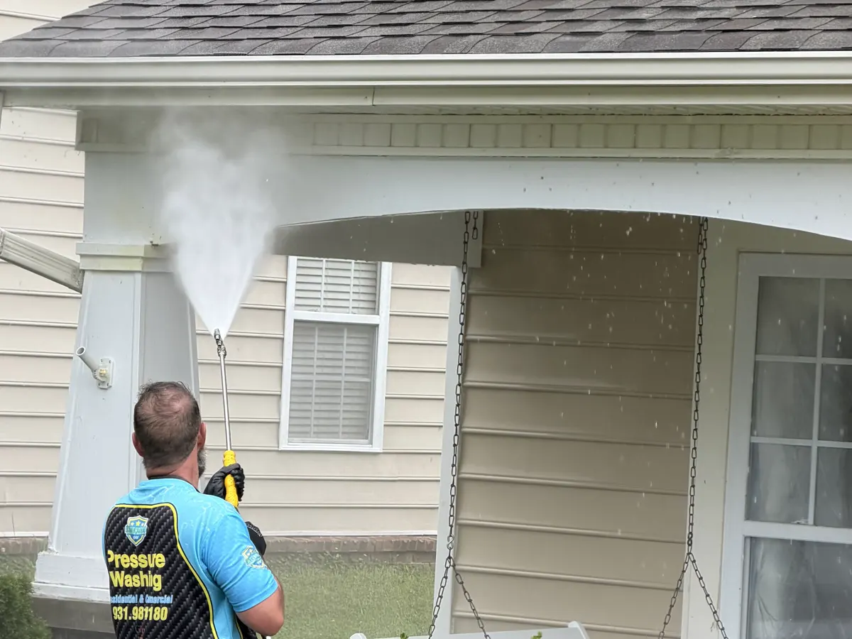 Soft wash rinse cleaning a porch column and soffit on a residential home.