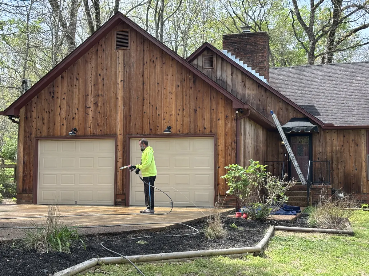 Technician rinsing a wood-sided garage during a house washing project.