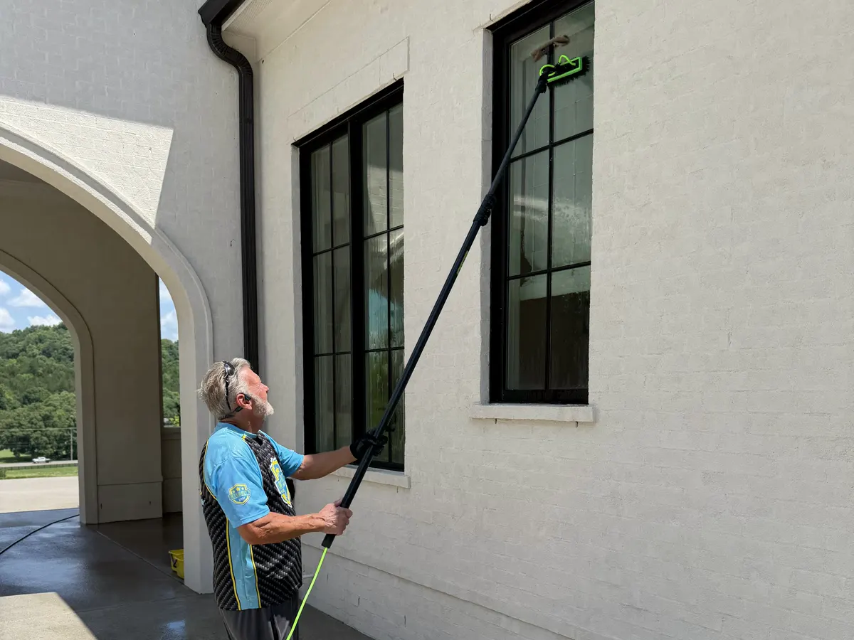 Soft washing a high exterior window and surrounding stucco with an extension pole.